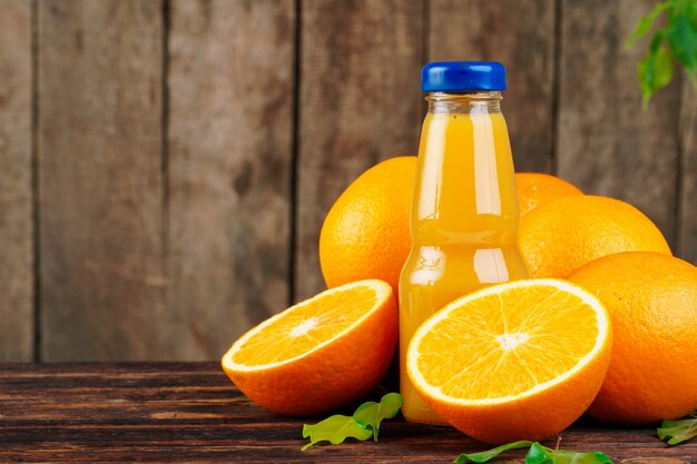 Garrafa de suco de laranja com laranjas na mesa de madeira