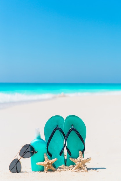 Garrafa de suncream, chinelos, estrela do mar e óculos de sol na praia de areia branca com vista para o mar
