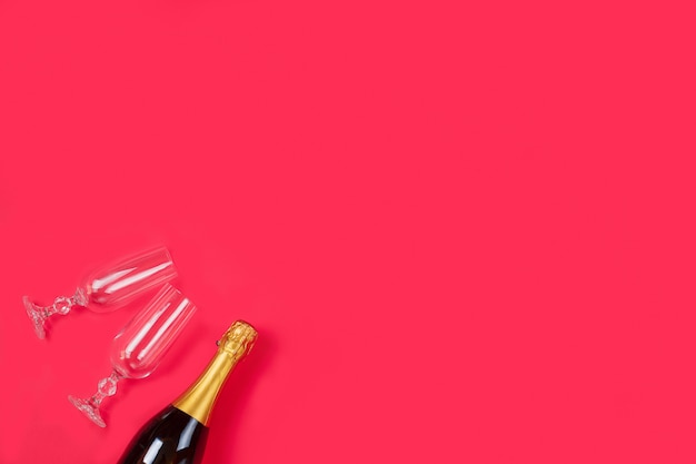 Garrafa de um champanhe e duas taças de champanhe em fundo vermelho.