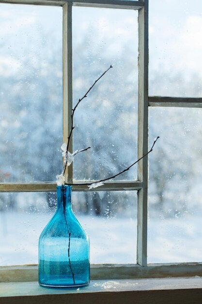 Garrafa de vidro azul com galho na velha janela de inverno