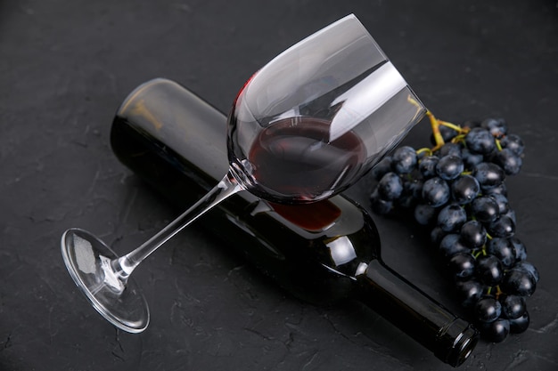 Foto garrafa de vidro com vinho e uvas escuras em um fundo escuro