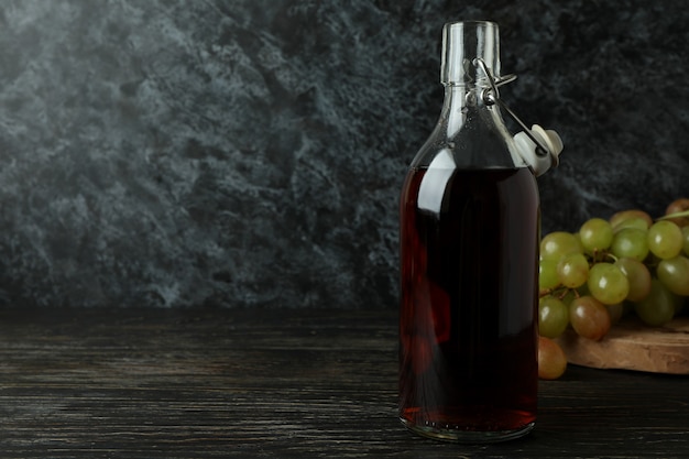 Garrafa de vinagre e uva na mesa de madeira rústica