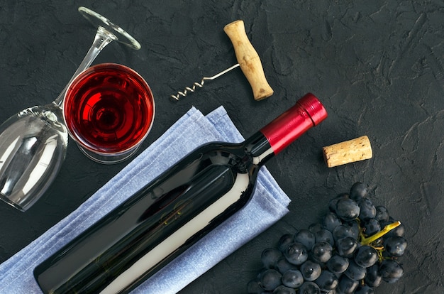 Garrafa de vinho, copo de vinho e cacho de uvas azuis na mesa escura. Vista do topo.