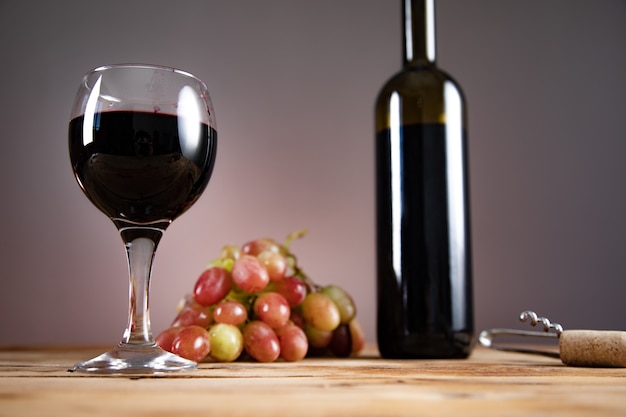 Garrafa de vinho de uvas e copo com abridor na mesa