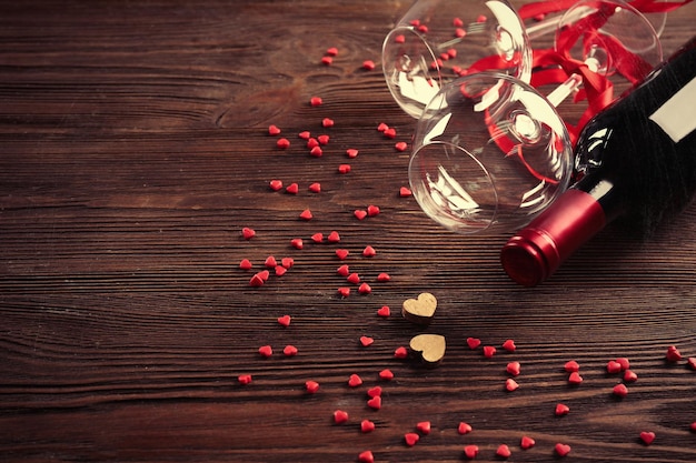 Garrafa de vinho e copos com corações artesanais em fundo de madeira
