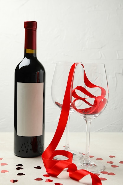 Garrafa de vinho e copos com glitter e fita na mesa texturizada branca
