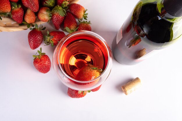 Garrafa de vinho rosa e uma taça de cristal junto com lindos morangos em uma superfície branca, foco seletivo.