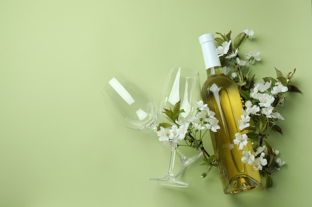 Garrafa de vinho, taças e flores sobre fundo verde