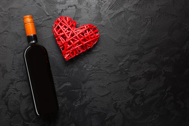 Garrafa de vinho tinto com coração decorativo de vime na mesa de pedra preta.