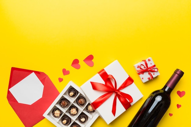 Garrafa de vinho tinto em fundo colorido para o dia dos namorados com envelope de caixa de presente e chocolate em forma de coração com caixa de presente de chocolates vista superior com espaço de cópia