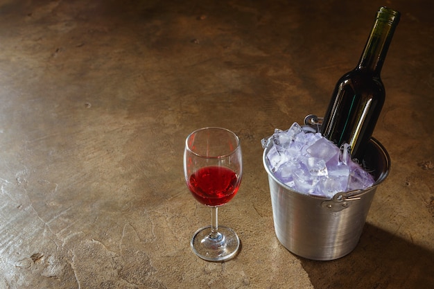 Garrafa de vinho tinto em um balde de gelo e uma taça de vinho tinto