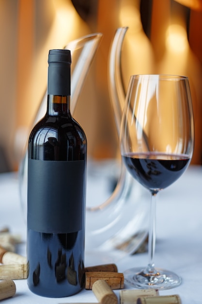 Garrafa de vinho tinto, um copo de vinho e uma jarra sobre uma mesa com uma toalha de mesa branca.