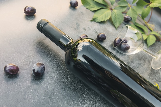 Garrafa de vinho tinto, videira verde, copo de vinho e uva madura no fundo da mesa de pedra escura vintage. Espaço de cópia de vista superior para texto. Adega de bar de vinhos de loja de vinhos ou conceito de degustação de vinhos.