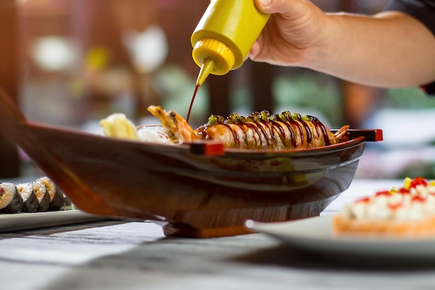 Garrafa derramando o molho sobre o sushi. aperte a garrafa na mão do homem. o japão envia saudações. uramaki rola do sushi café.