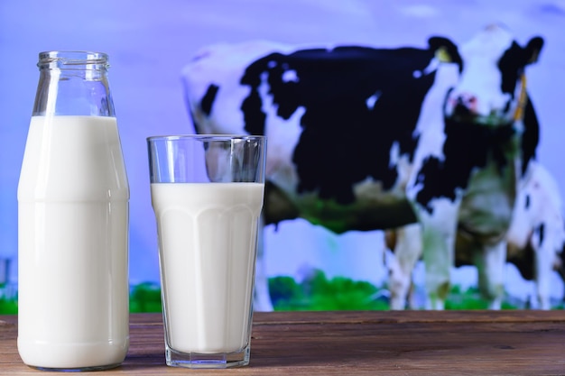 garrafa e copo com leite em uma mesa de madeira imagem de vaca em um pasto ao fundo