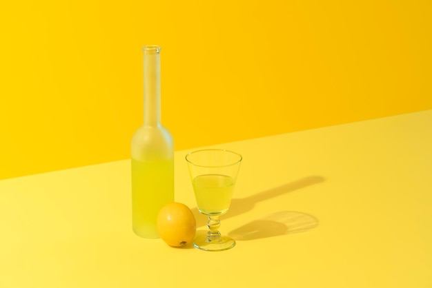 Garrafa e copo de licor de limão limoncello em um fundo amarelo bebida italiana feita com limões