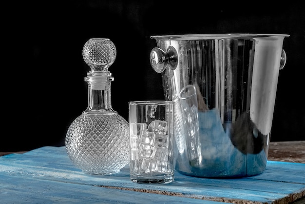 Garrafa e vidro vazios do cubo de gelo no fundo de madeira azul da tabela.