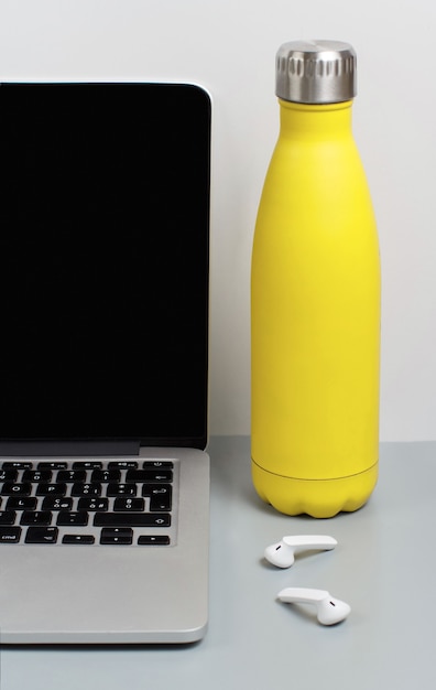Garrafa isolada amarela na mesa cinza perto do laptop close-up