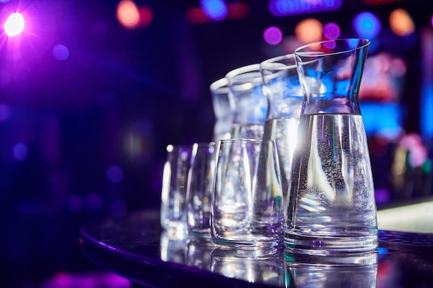 Garrafas con agua y vasos en el bar de una discoteca frente a focos multicolores