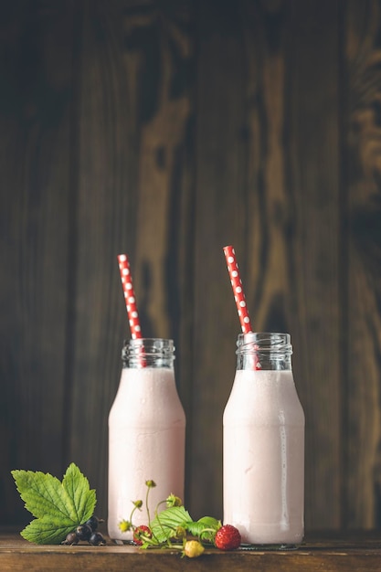 Garrafas com delicioso milk-shake de morango ou smoothie com ramo de morango silvestre na mesa de madeira escura e fundo