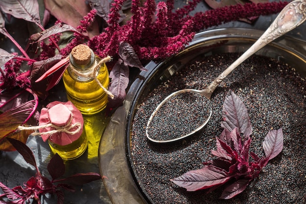 Garrafas com óleo de amaranto, plantas e sementes de amaranto em uma superfície escura