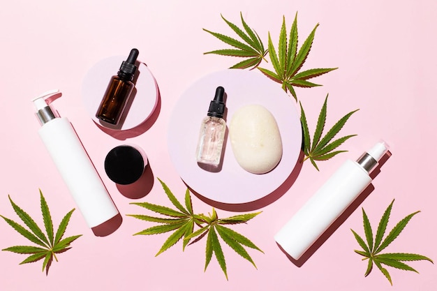 Garrafas com tinta de óleo CBD THC e folhas de cannabis em fundo rosa Cosméticos alternativos