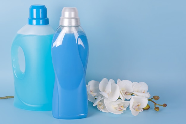 Garrafas de amaciante de detergente e tecido com flores da orquídea em fundo azul