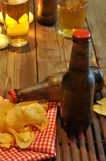 Garrafas de cerveja gelada e batatas fritas na mesa de madeira