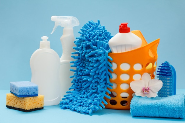 Garrafas de detergente líquido trapos uma cesta e esponjas sobre fundo azul