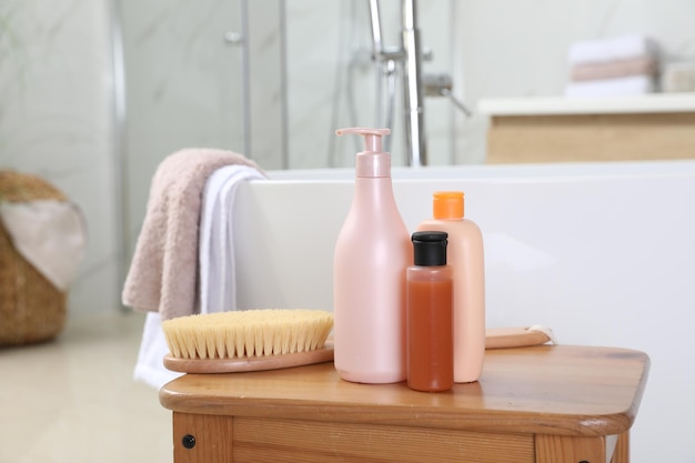 Garrafas de gel de banho e escova na mesa de madeira perto da banheira no espaço do banheiro para texto