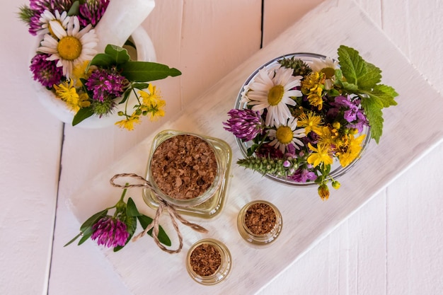 Garrafas de vidro de óleo de erva de São João orgânico ficam em uma mesa de almofariz e pilão de tábuas de madeira brancas com medicina alternativa de flores de grama