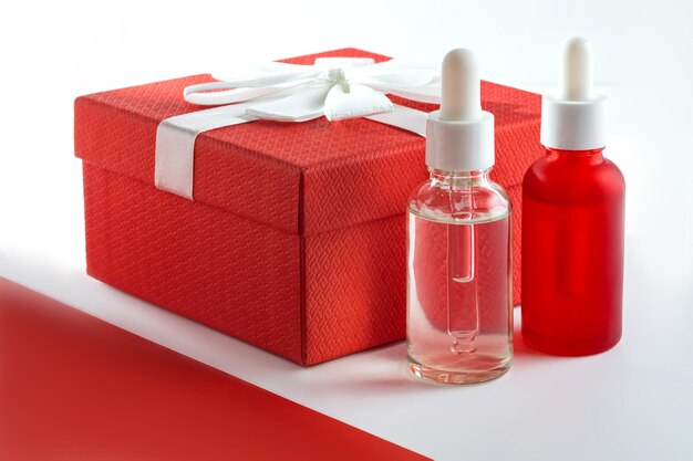 Garrafas de vidro de soro com pipeta em fundo branco e caixa de presente vermelha com laço de fita Cosméticos de Spa Orgânicos Naturais Conceito de moda Presente para férias