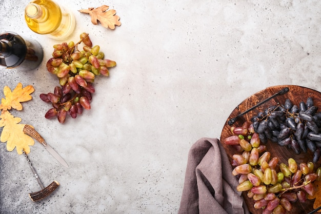 Garrafas de vinho com uvas e um copo de vinho no antigo fundo de mesa de concreto cinza com espaço de cópia. Vinho tinto com um galho de videira. Composição do vinho em fundo rústico. Brincar.