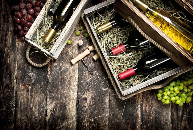 Garrafas de vinho tinto e branco em velhas caixas na mesa de madeira.