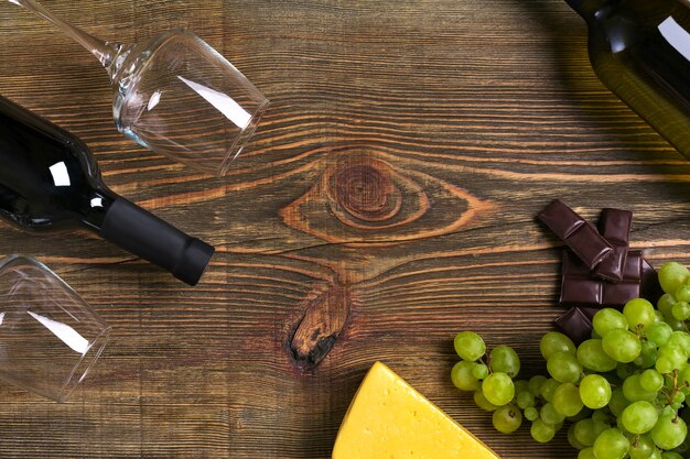 Garrafas de vinho tinto e branco, uva, queijo e copos sobre a mesa de madeira. Vista superior com espaço de cópia. Ainda vida. Postura plana