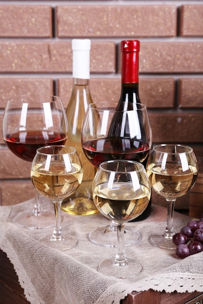 Garrafas e copos de vinho e uvas maduras na mesa no fundo da parede de tijolo