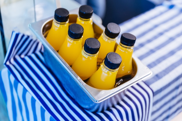 Garrafas frias do suco de laranja na caixa de alumínio na tela branca e azul da tira.