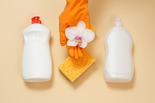 Garrafas plásticas de esponjas líquidas para lavar louça e flor de orquídea branca na mão em uma luva de borracha