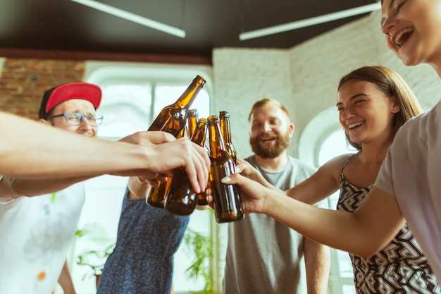 Garrafas tilintando. Grupo de jovens amigos bebendo cerveja, se divertindo, rindo e comemorando juntos. Mulheres e homens com copos de cerveja. Oktoberfest, amizade, união, conceito de felicidade.