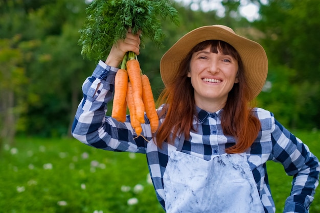 Gartenarbeit - Schöne junge Frau mit Bio-Karotten in einem Gemüsegarten. Hintergrundbeleuchtung