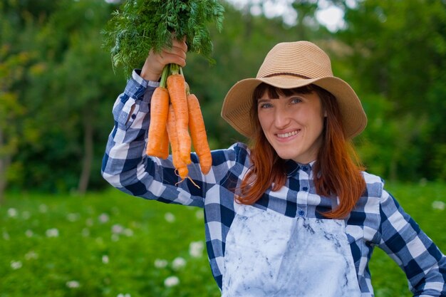 Gartenarbeit - Schöne junge Frau mit Bio-Karotten in einem Gemüsegarten. Hintergrundbeleuchtung