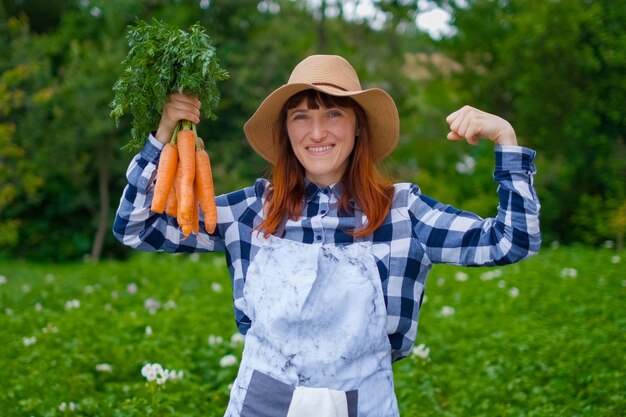 Gartenarbeit - Schöne junge Frau mit Bio-Karotten in einem Gemüsegarten. Hintergrundbeleuchtung