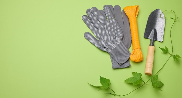 Gartengeräte für die Verarbeitung von Beeten im Garten und Textilhandschuhe auf grünem Hintergrund