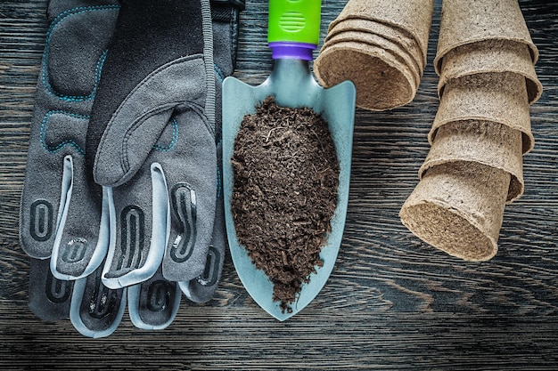 Gartenhandspaten Erde Torftöpfe Schutzhandschuhe auf Holzbrett.