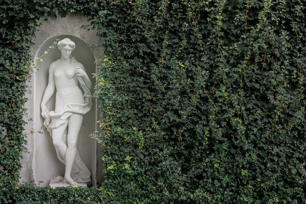 Foto gartenskulptur ein wunderschöner sockel einer frau auf dem hintergrund einer grünen wand im park. hintergrund für veranstaltungen im freien