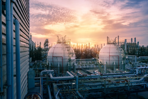 Gasspeicherkugeltanks und Rohrleitung in der petrochemischen Industrieanlage auf Hintergrund des Sonnenuntergangs am Himmel, Herstellung der Erdölindustrieanlage