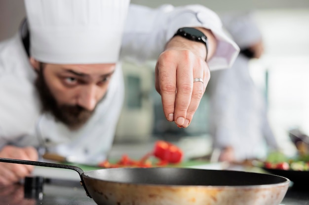 Gastronomieexperte bereitet Gericht mit frischem und biologischem Gemüse in der Küche zu. Gourmet-Küchenchef garniert Abendessen mit rotem Paprika, während er Speisen für gehobene Küche im Restaurant kocht