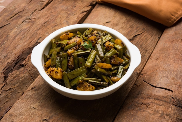 Gawar ki sabzi - Frijoles en racimo al curry con patatas y especias servido en un cuenco sobre un fondo de mal humor. Enfoque selectivo