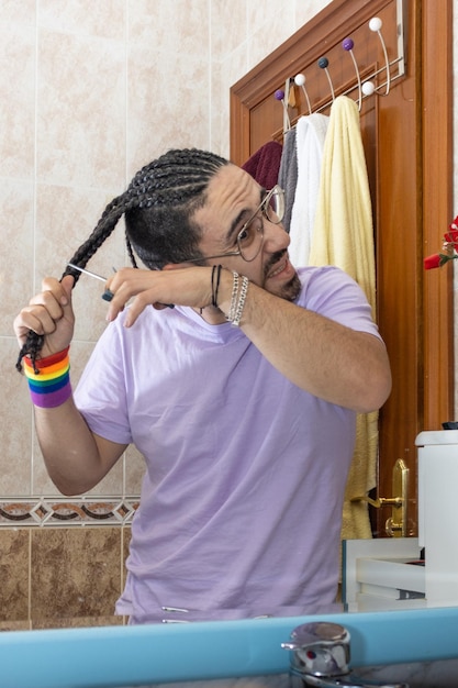 Gay de trança cortando o cabelo na frente do espelho Gay cortando o cabelo com tesoura Pessoa cortando o próprio cabelo na frente do espelho