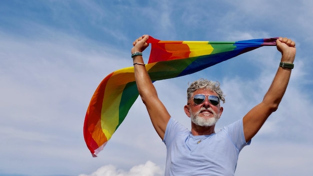 Gay grisalho segura bandeira LGBT contra um céu